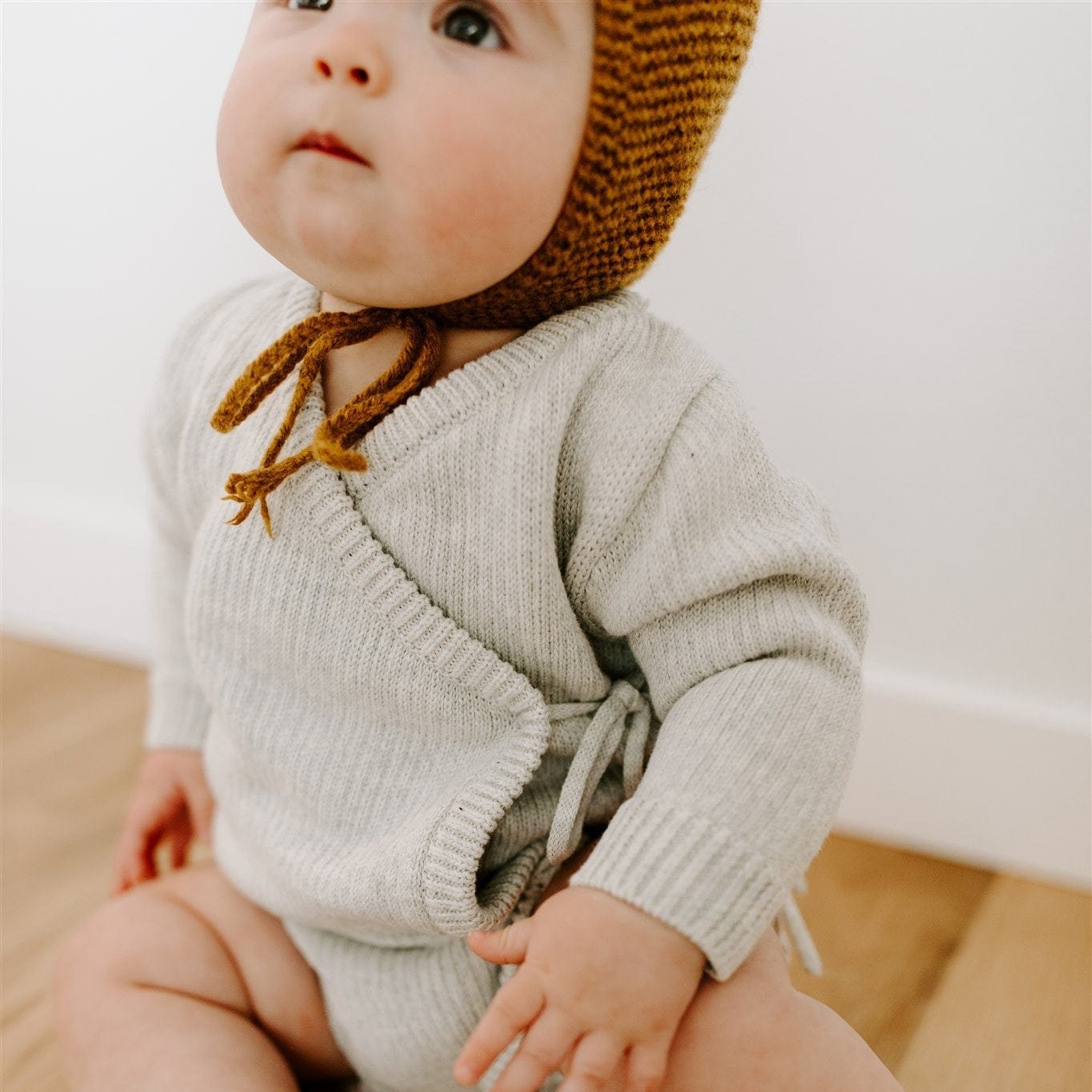 Oaklyn bodysuit in an airy neutral dove gray, featuring a whimsical kimono-style tie closure and snap buttons for easy diaper changes. Soft cotton yarn fabric for baby’s comfort, perfect for winter wardrobes.