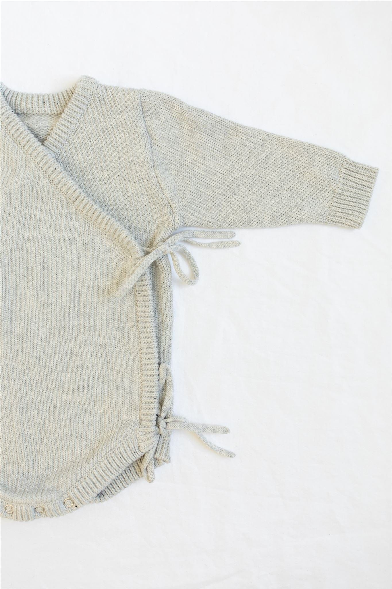 Oaklyn bodysuit in an airy neutral dove gray, featuring a whimsical kimono-style tie closure and snap buttons for easy diaper changes. Soft cotton yarn fabric for baby’s comfort, perfect for winter wardrobes.